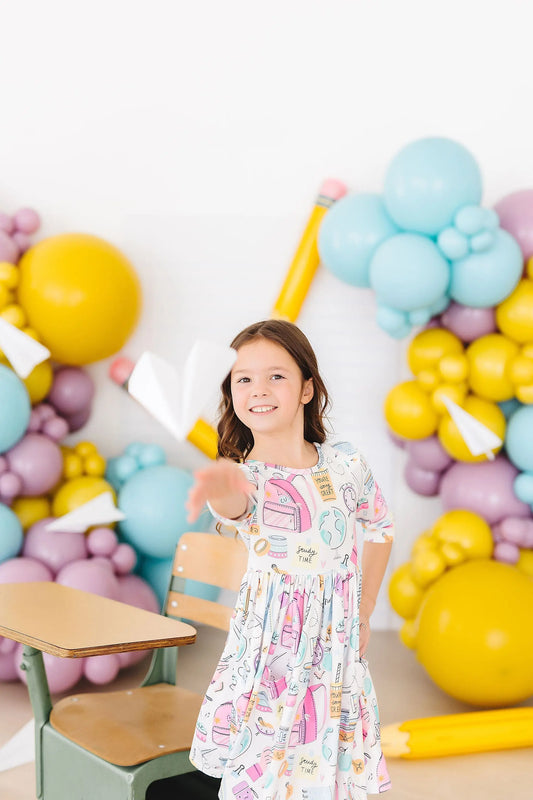 Young girl in a patterned dress standing in front of a colorful balloon arch.