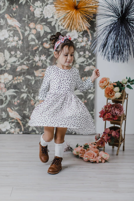 Young girl in a polka dot dress standing in a decorated room with floral decorations and a floral-patterned wall.