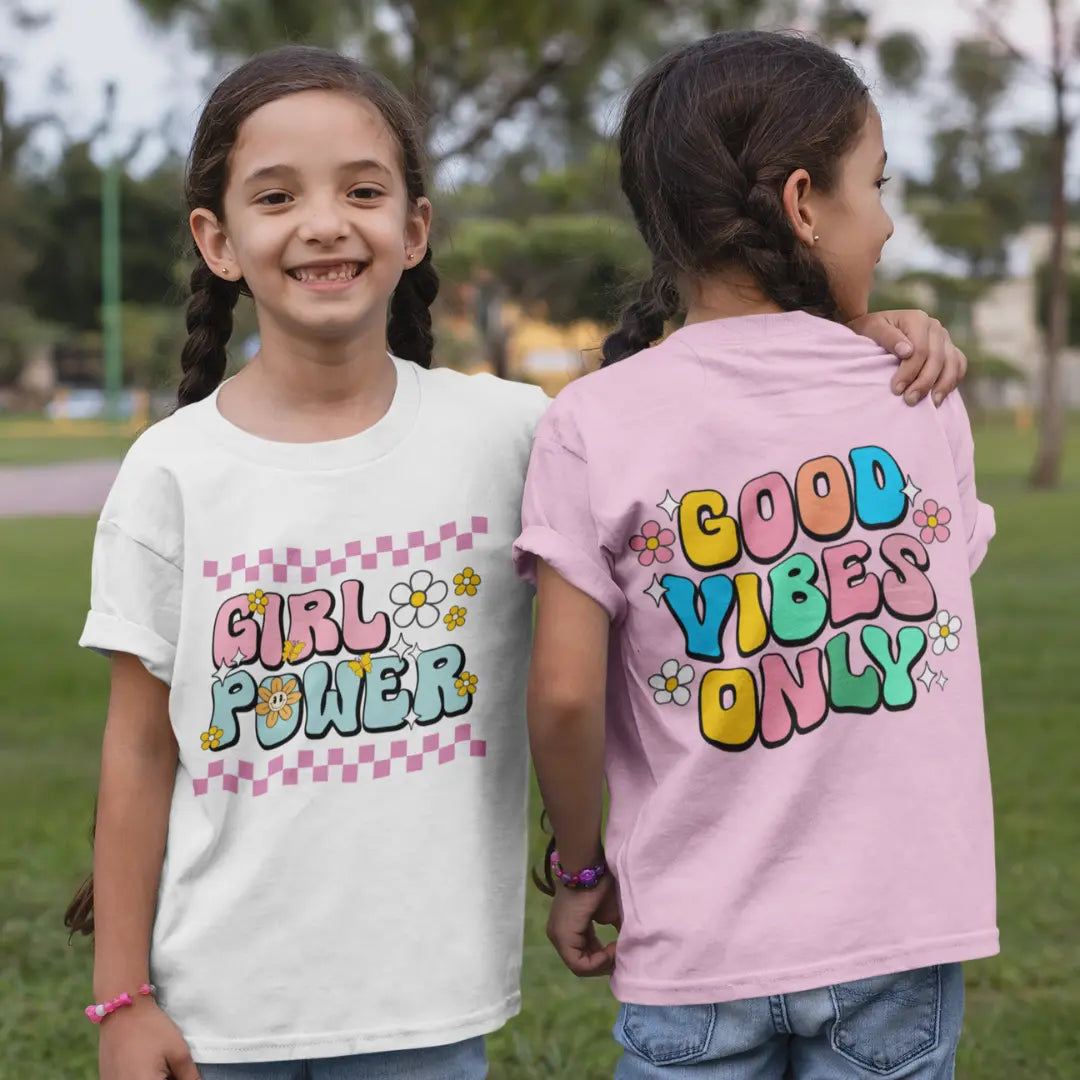 Two children wearing t-shirts with motivational phrases, one in a park setting.