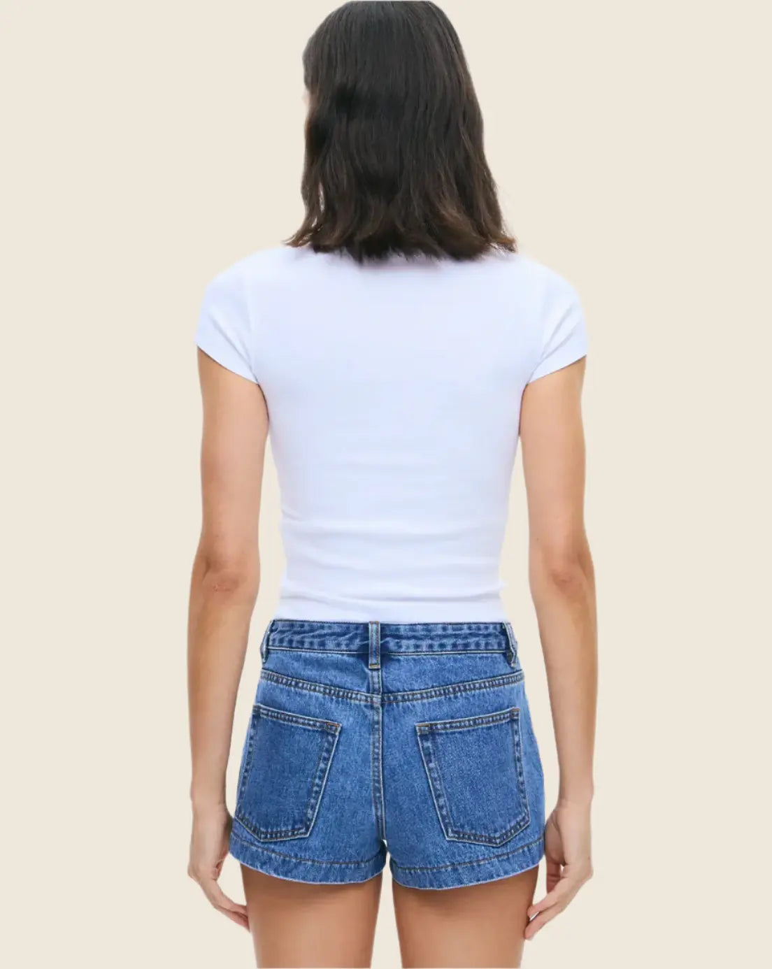 Person wearing a white t-shirt and blue denim shorts on a beige background
