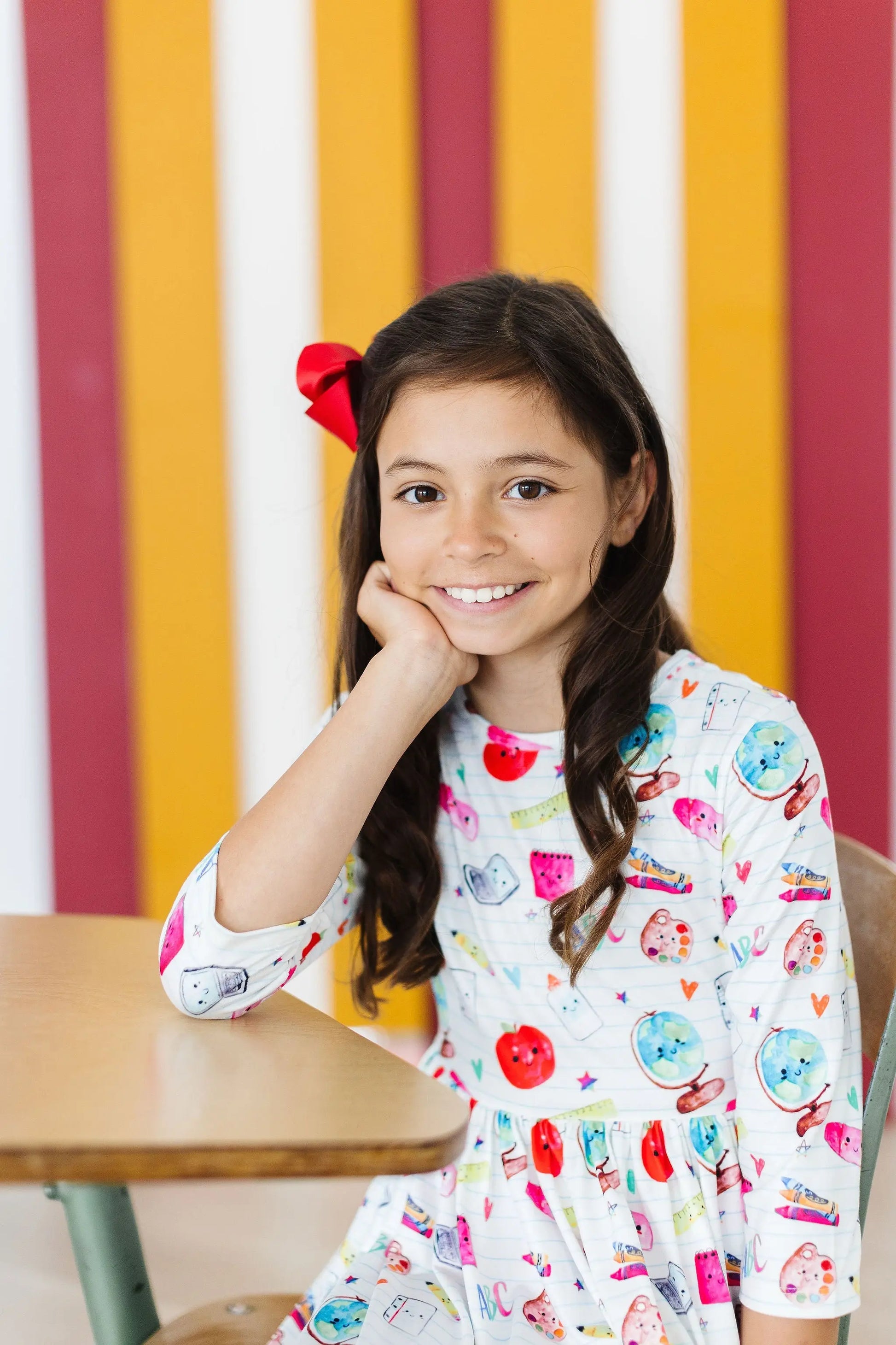 Young girl sitting at a desk with a colorful striped background