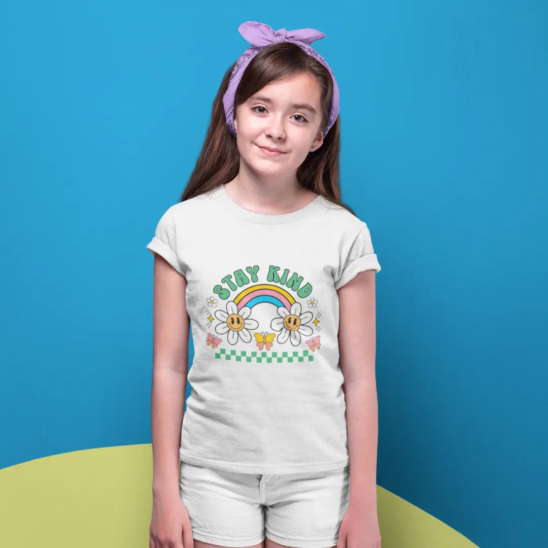 Young girl wearing a white t-shirt with a rainbow design and the text  stay kind against a blue background