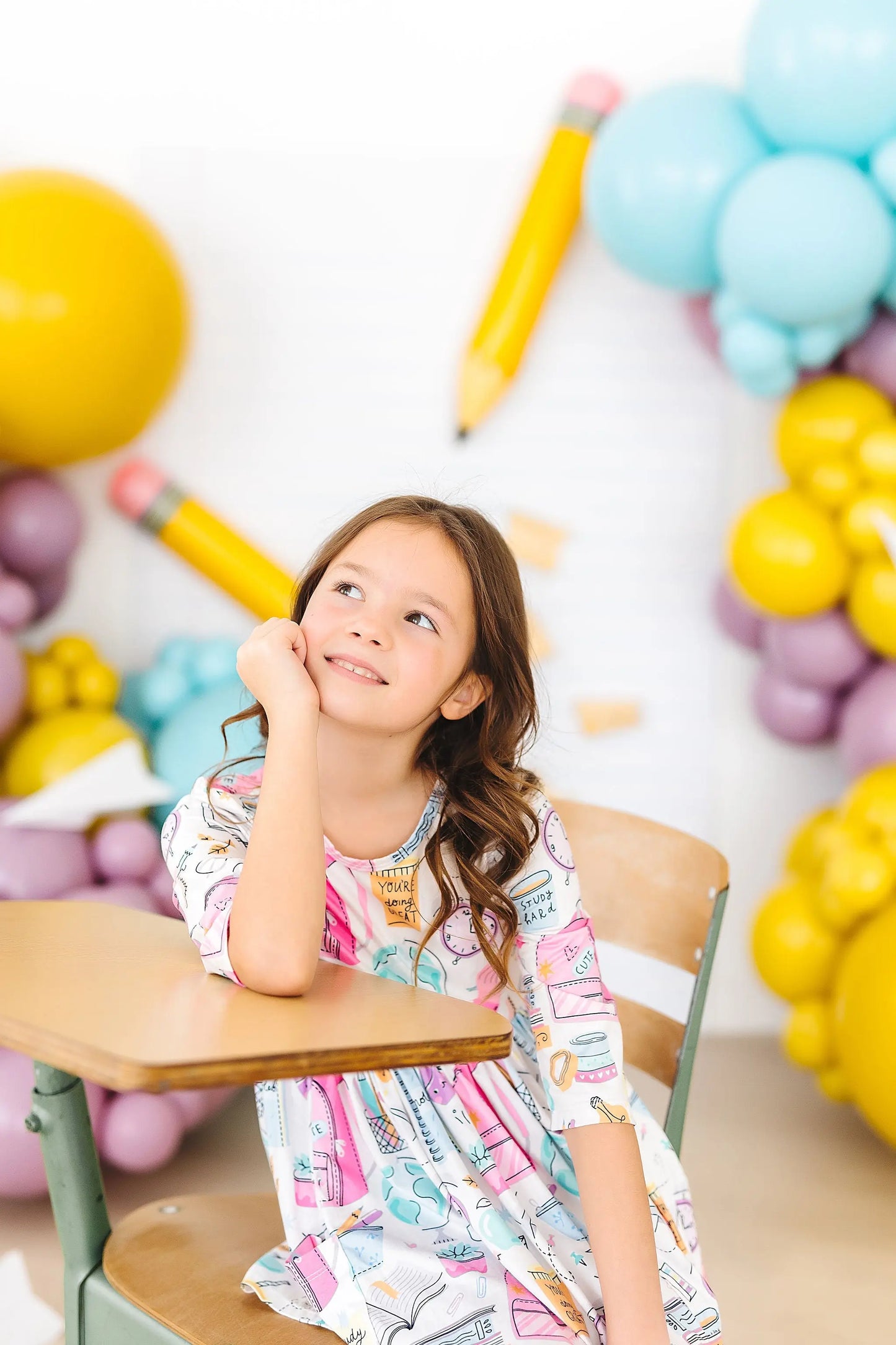 Young girl sitting at a desk with colorful balloons and pencils in the background