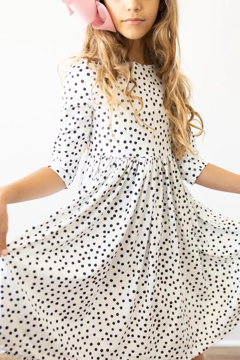 Young girl wearing a white dress with black polka dots on a plain background