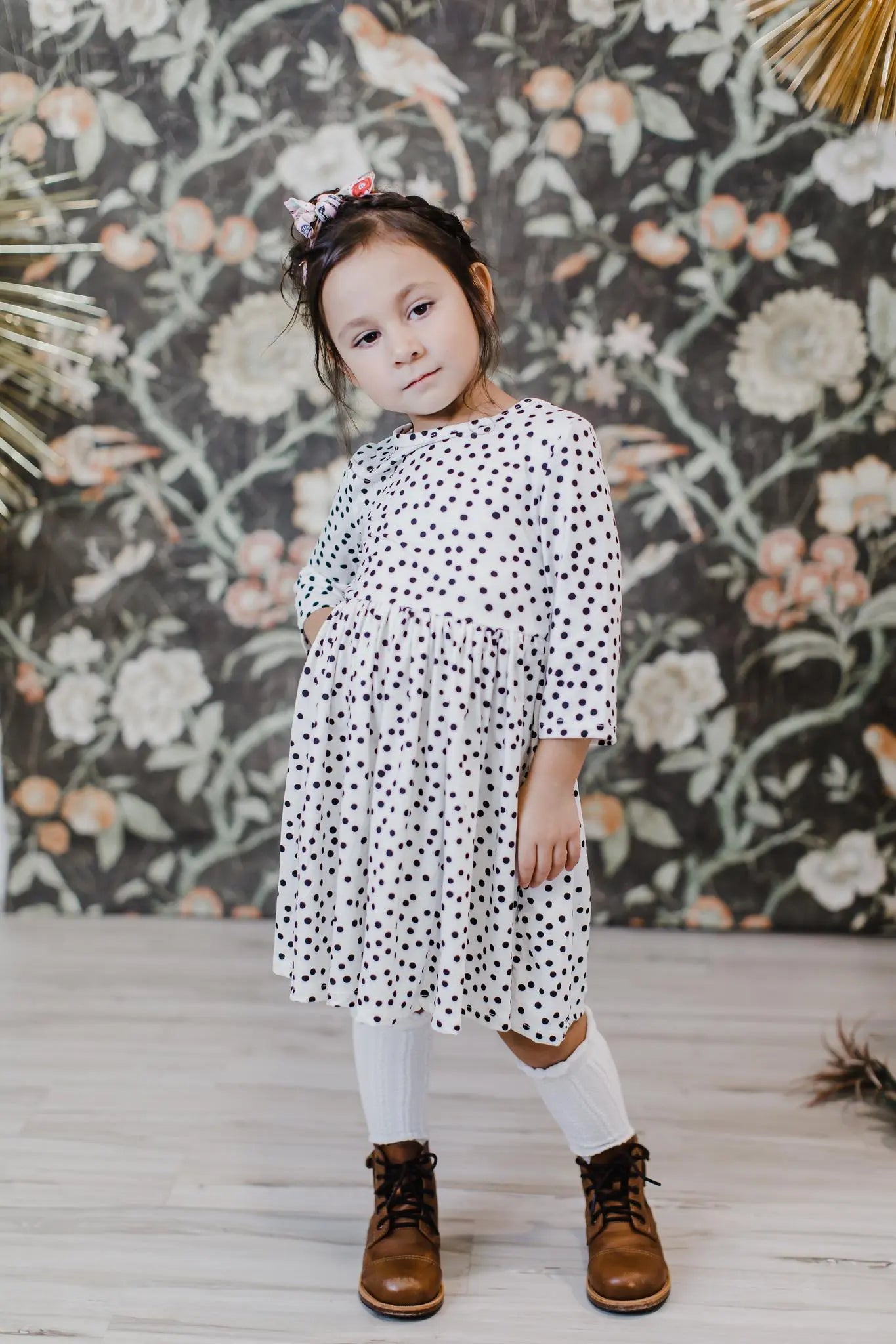 Child wearing a polka dot dress with floral wallpaper in the background