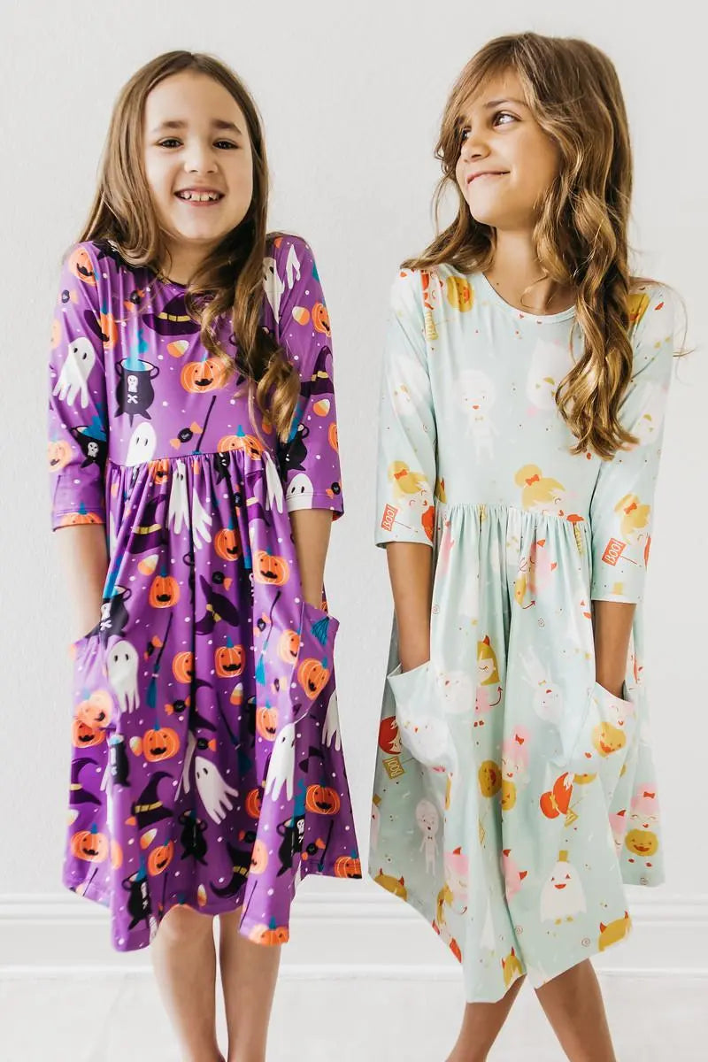 Two children wearing Halloween patterned dresses standing side by side on a white background