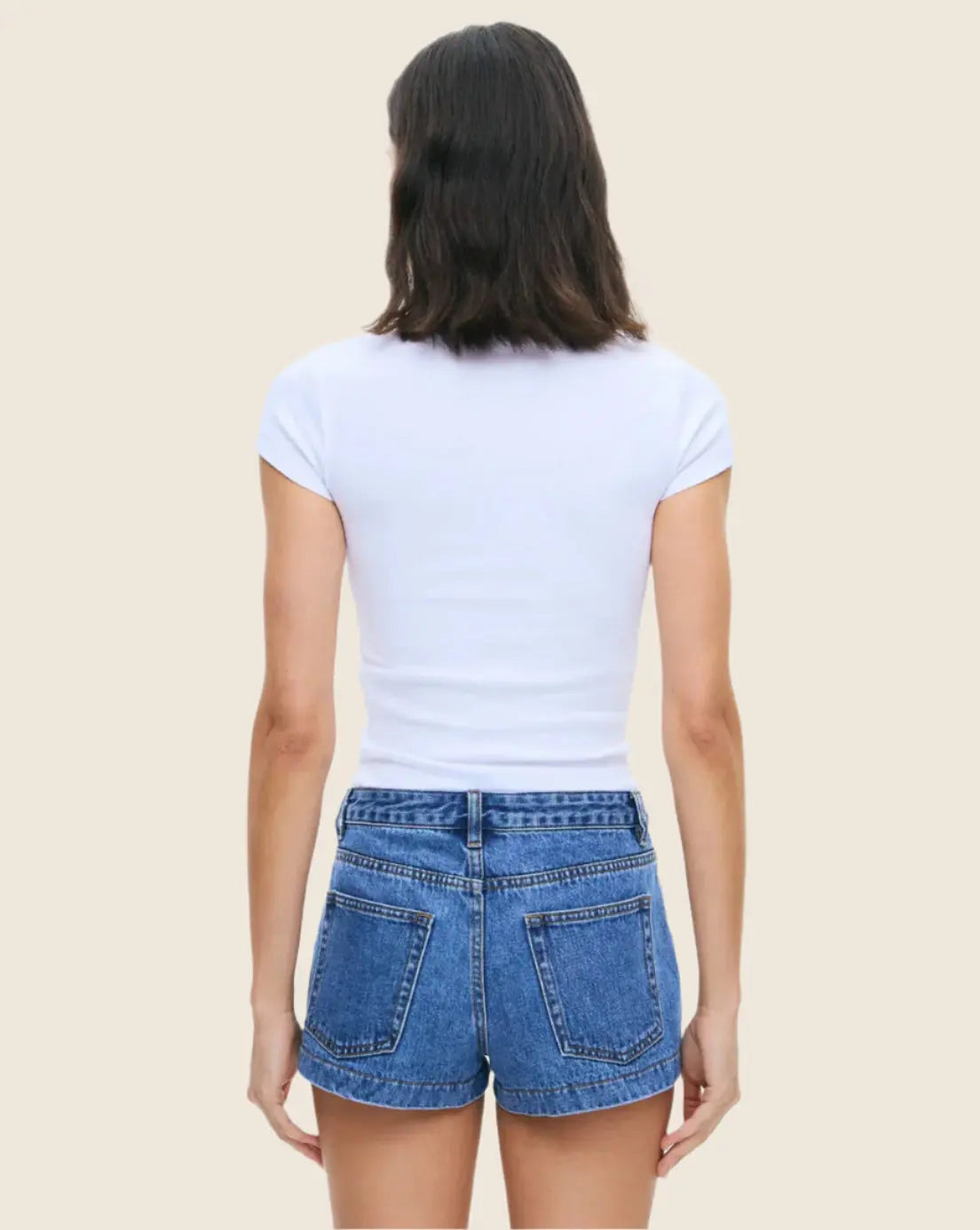 Person wearing a white t-shirt and blue denim shorts on a beige background