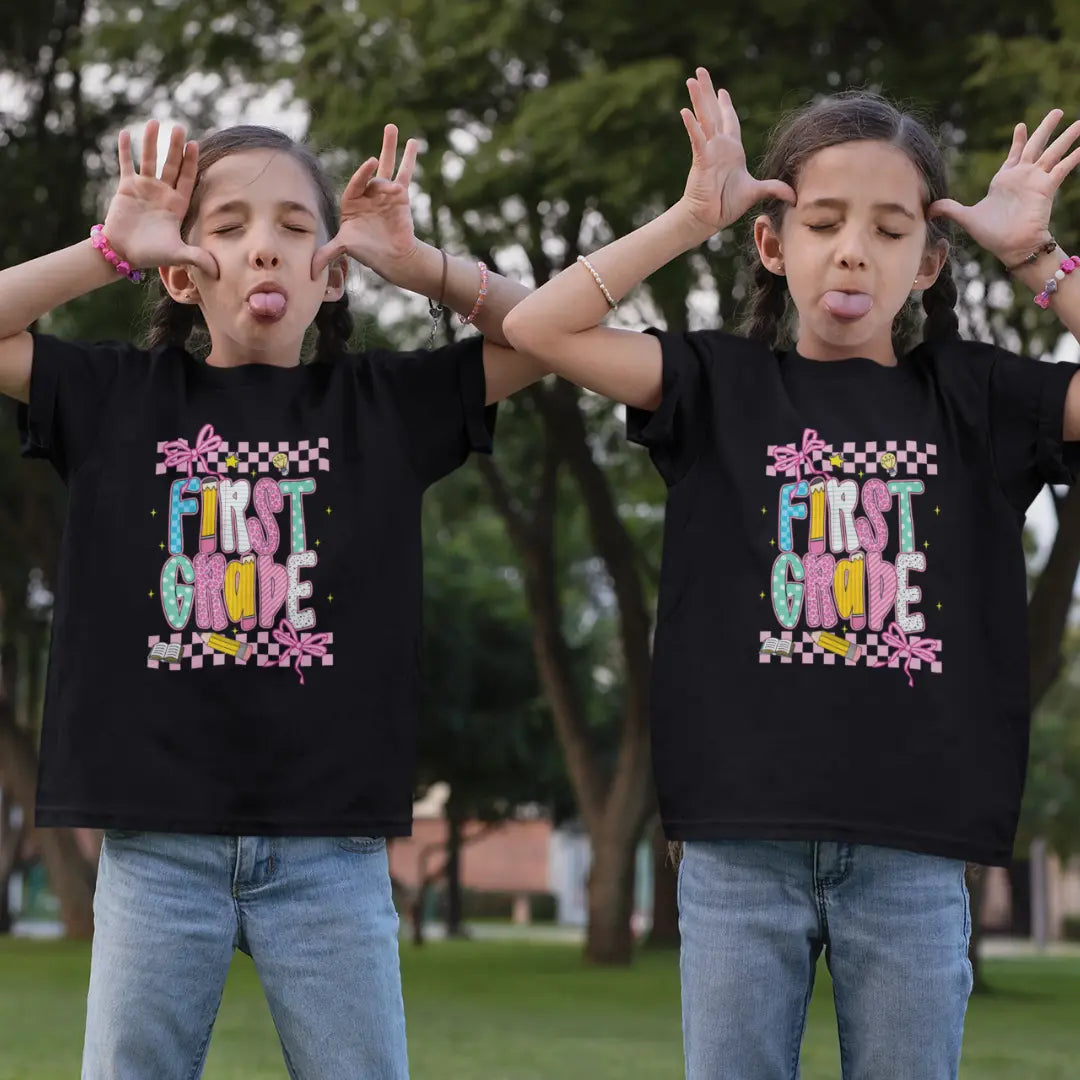 Two children wearing black 'First Grade' t-shirts outdoors.