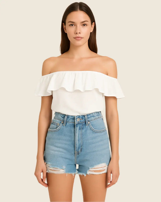 Woman wearing a white off-shoulder top and denim shorts on a beige background