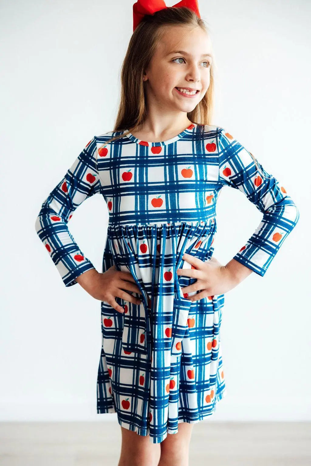 Girl wearing a blue plaid dress with red apple print on a white background