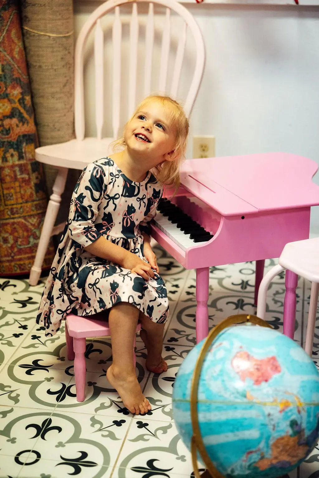 Child sitting on a pink chair next to a small pink piano with a globe in the foreground.